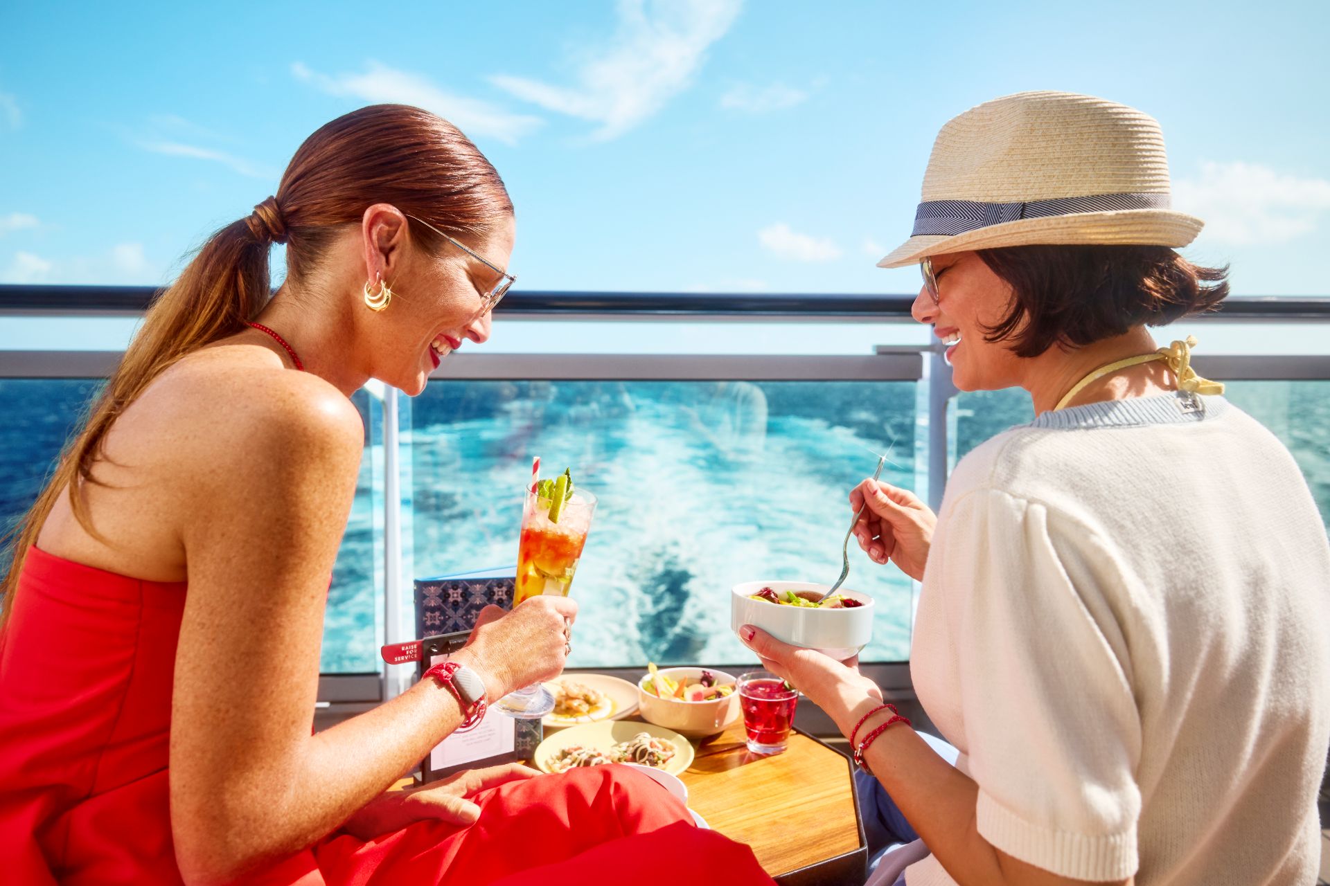 Two friends sharing a meal and cocktails on deck by the ocean